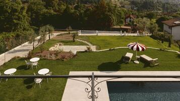 A poolside area with a view of a village, outdoor seating, and a well-maintained lawn.