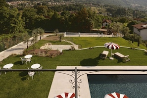 A poolside area with a view of a village, outdoor seating, and a well-maintained lawn.