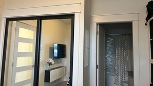 Un espacio interior con una puerta corredera que da a un baño, un televisor de pantalla plana montado en un mueble, y un inodoro con cortina de ducha estampada.