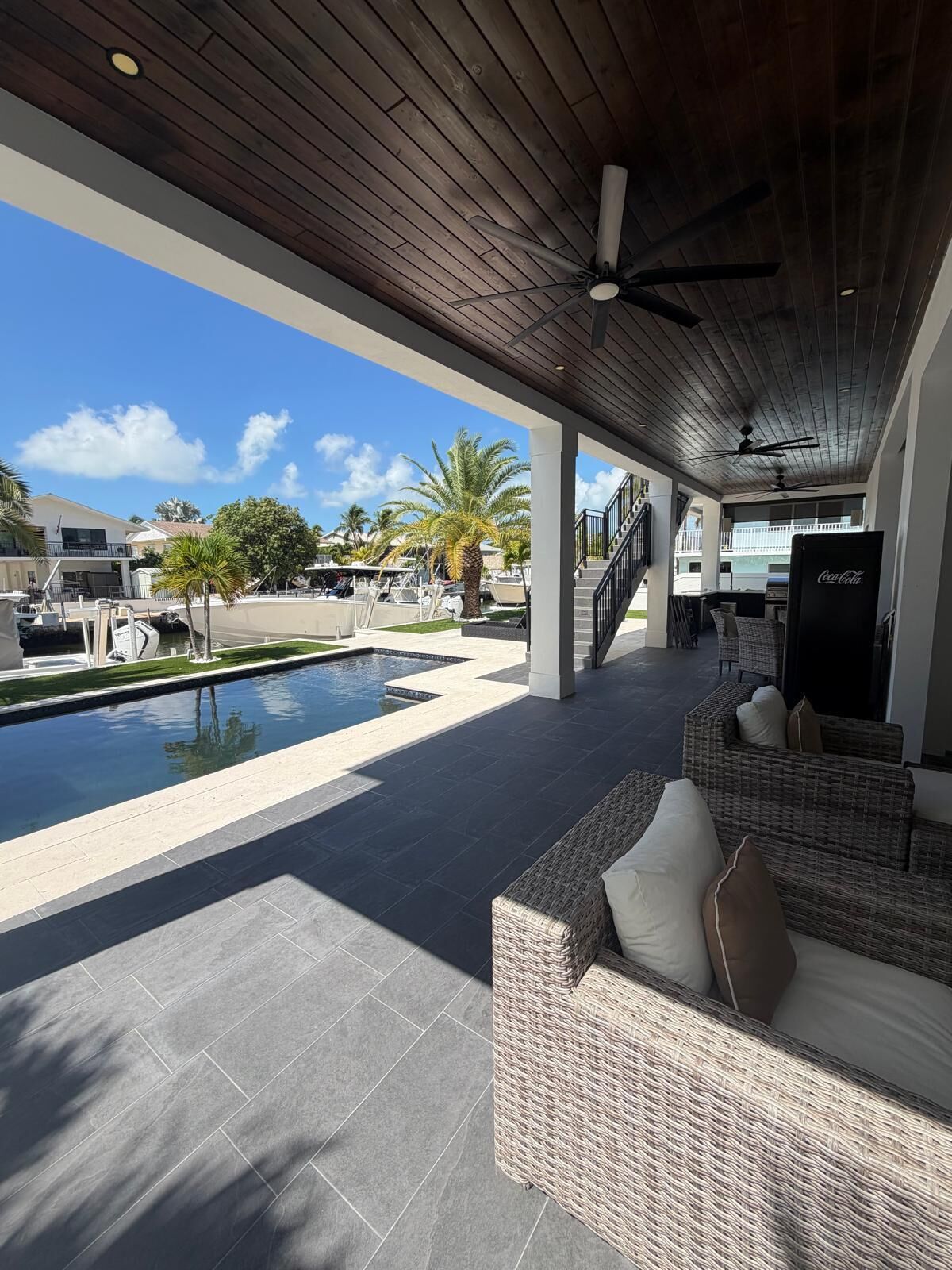 A covered outdoor area with a pool, wicker furniture, and a Coca-Cola refrigerator.