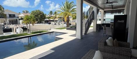 A covered outdoor area with a pool, wicker furniture, and a Coca-Cola refrigerator.