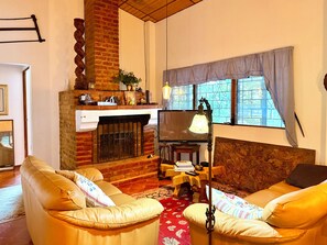 Ein Wohnzimmer mit Ledersofas, einem Kamin, einem Fernseher und einem Fenster mit Vorhängen.