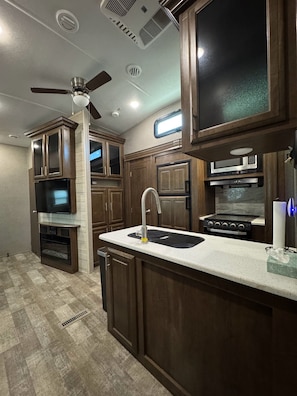 A modern kitchen with wooden cabinets, a stainless steel sink, a microwave, and a stove. - Wonderful 2-bedroom recreational vehicle with AC in Fairfield (Fairfield)