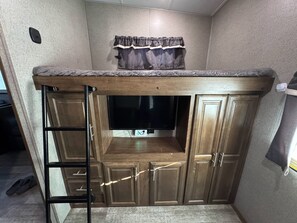 A bunk bed with a ladder, wooden cabinets, and a small window with curtains. - Wonderful 2-bedroom recreational vehicle with AC in Fairfield (Fairfield)