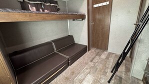 Ein kleines Zimmer mit Etagenbett, einer kleinen Bank und einer Tür mit Kleiderhaken.