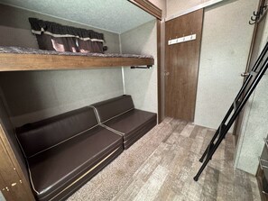 A compact room with a bunk bed, a small bench, and a door with a coat rack. - Wonderful 2-bedroom recreational vehicle with AC in Fairfield (Fairfield)