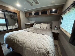 A bedroom with a bed, a nightstand, a dresser, and a window with blinds.