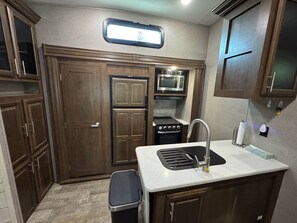 A compact kitchen with wooden cabinets, a microwave, a stove, and a sink. - Wonderful 2-bedroom recreational vehicle with AC in Fairfield (Fairfield)