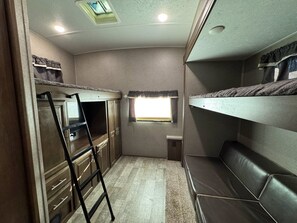 Een compact camperinterieur met stapelbedden, een kitchenette en een klein raam.