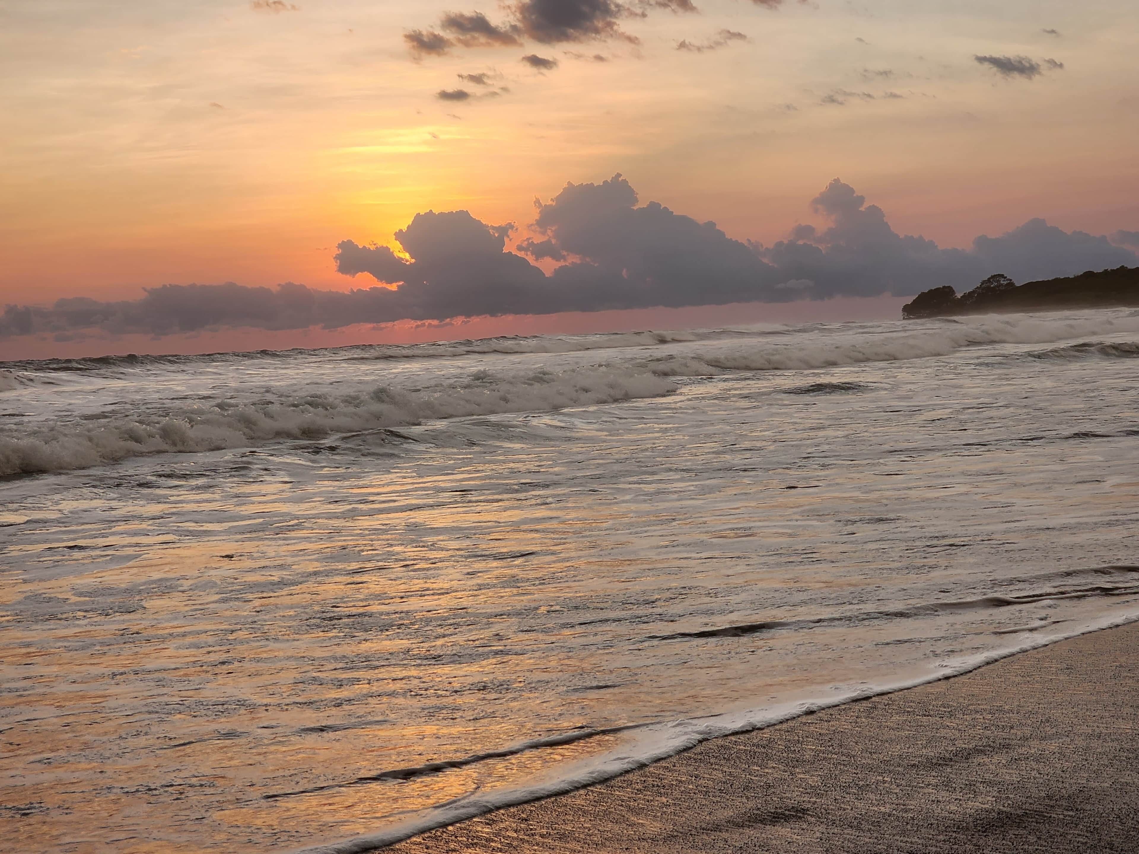 A beach with waves and a sunset.