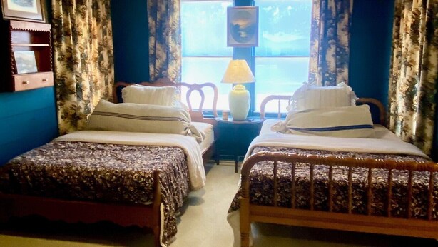 Een kamer met twee bedden, een raam met gordijnen, een lamp en een plafondventilator.