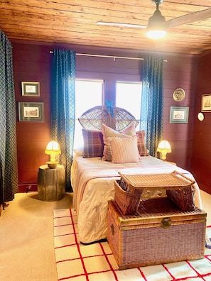 A cozy bedroom with a bed, two bedside lamps, a window with curtains, and a ceiling fan.