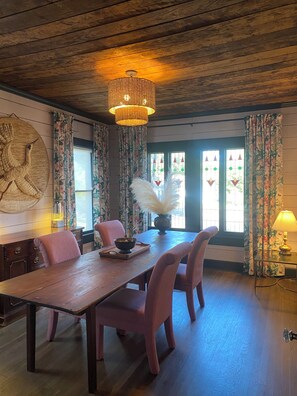 A dining area with a wooden table, four chairs, a chandelier, and floral curtains.