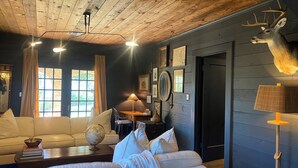 Een gezellige woonkamer met een houten plafond, een opgehangen hertenkop en een wereldbol op de bank.