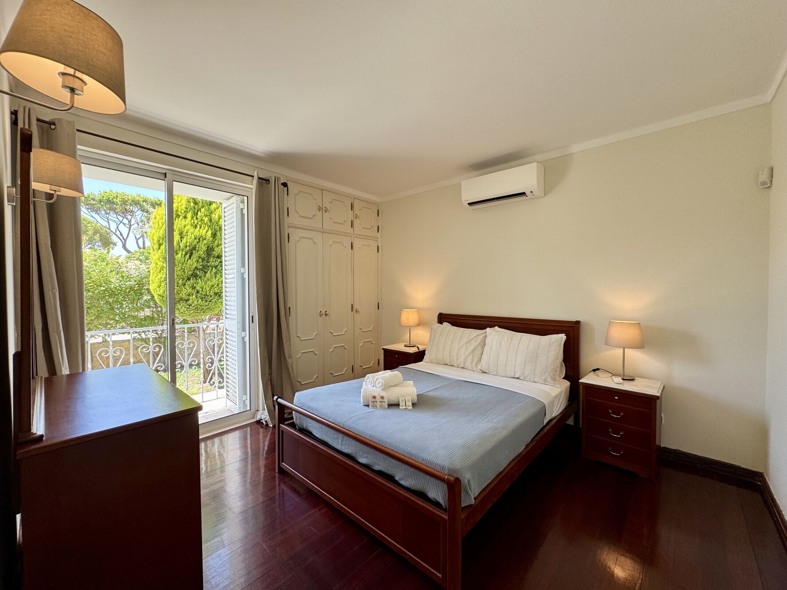 A bedroom with a wooden bed, two bedside tables, a wardrobe, and a balcony with curtains.