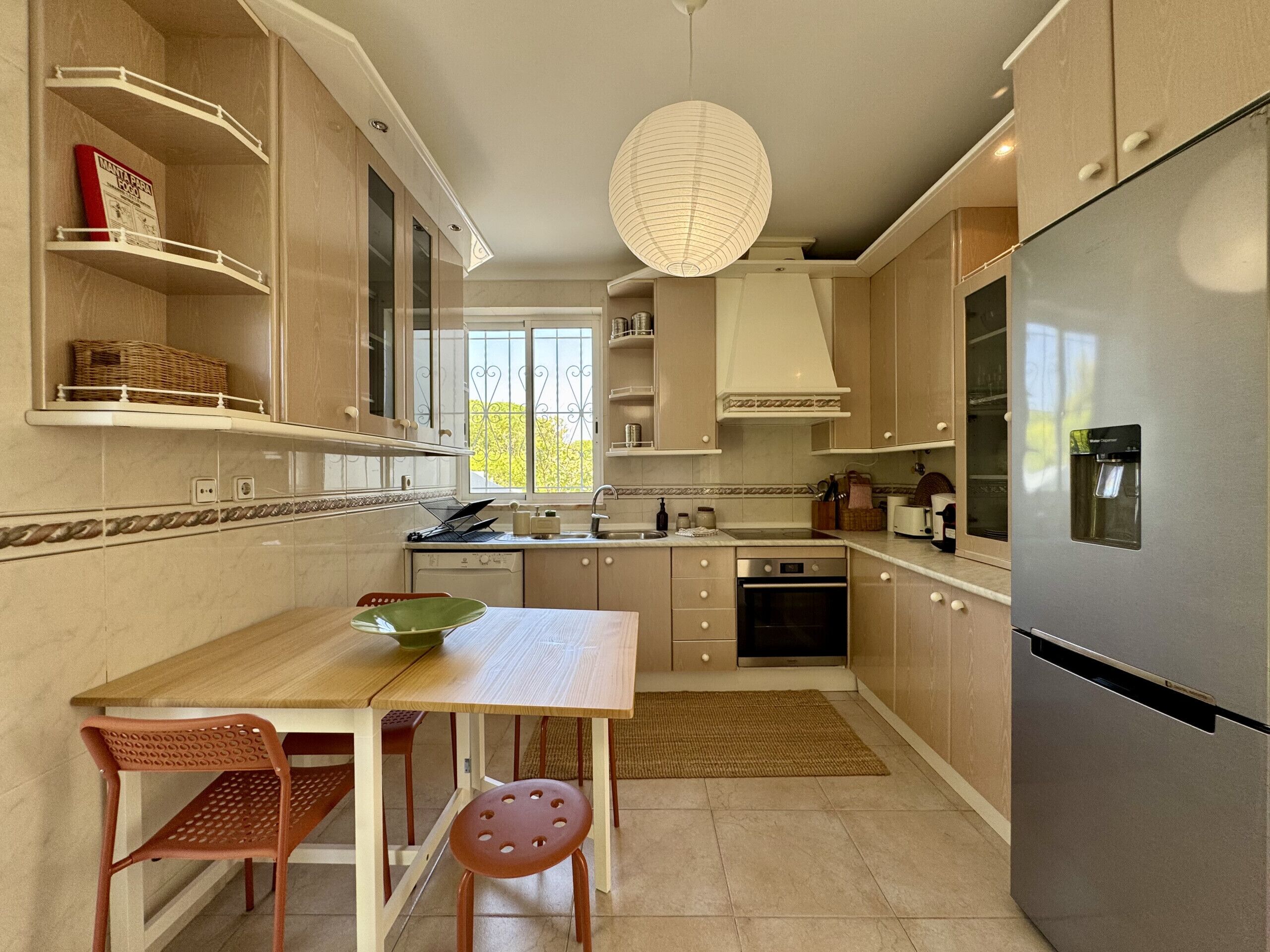 A modern kitchen with a dining table, chairs, a refrigerator, and a hanging light fixture.