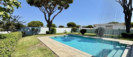A swimming pool with a water feature, surrounded by a well-maintained lawn and trees.