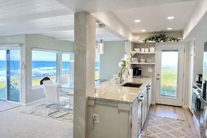 Una cocina moderna con una isla grande, un comedor con vista al océano y una sala de estar amplia con un gran ventanal con vista a la playa.