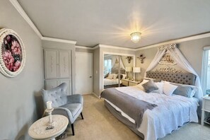 Une chambre à coucher avec un grand lit, un coin salon comprenant une chaise et une table, une armoire et un miroir.