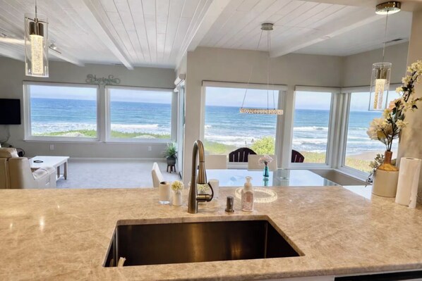 A modern kitchen with a large island, a sink, and a view of the ocean through large windows.