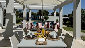 A covered outdoor dining area with tables set for breakfast, overlooking a swimming pool. - VILAMOURA SUN & BEACH VILLA WITH POOL by HOMING (Vilamoura)