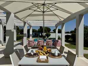 A covered outdoor dining area with tables set for breakfast, overlooking a swimming pool. - VILAMOURA SUN & BEACH VILLA WITH POOL by HOMING (Vilamoura)