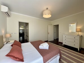 Habitación de hotel con cama, cómoda, espejo y puerta que da a un pasillo.