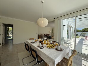 A dining area with a table set for breakfast, chairs, and a large window with a view. - VILAMOURA SUN & BEACH VILLA WITH POOL by HOMING (Vilamoura)