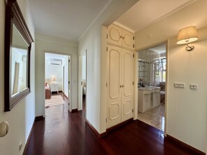 A hallway with a wooden floor, a white door, and a bathroom visible through an open door. - VILAMOURA SUN & BEACH VILLA WITH POOL by HOMING (Vilamoura)