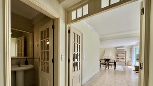 A hallway with a bathroom on the left, a dining area with chairs and a table in the center, and a fireplace with a bookshelf in the background. - VILAMOURA SUN & BEACH VILLA WITH POOL by HOMING (Vilamoura)
