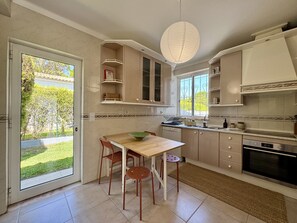 A modern kitchen with a dining area, a large window, and a view of a garden. - VILAMOURA SUN & BEACH VILLA WITH POOL by HOMING (Vilamoura)