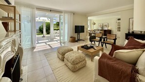 A spacious living room with a fireplace, a television, and a dining area visible through the glass doors. - VILAMOURA SUN & BEACH VILLA WITH POOL by HOMING (Vilamoura)