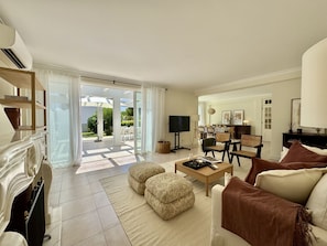 A spacious living room with a fireplace, a television, and a dining area visible through the glass doors. - VILAMOURA SUN & BEACH VILLA WITH POOL by HOMING (Vilamoura)