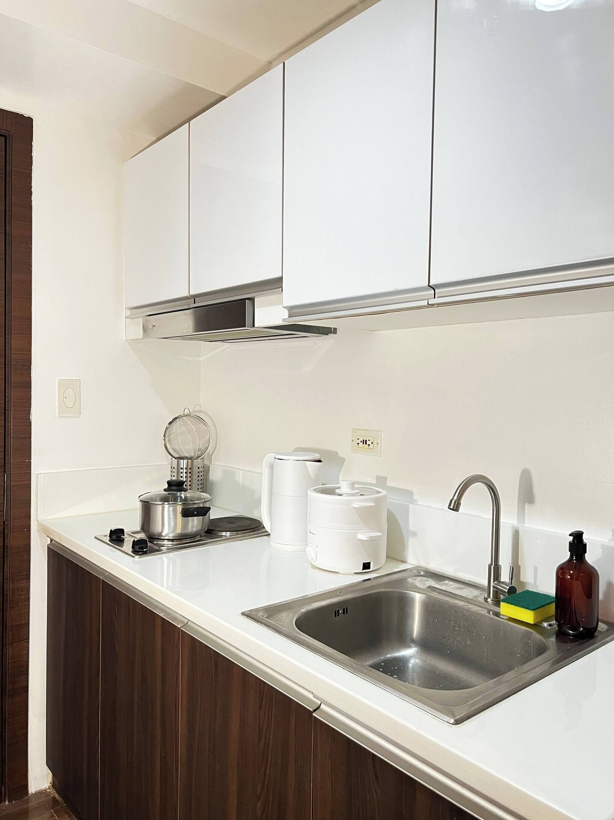 A kitchen with white cabinets, a stainless steel sink, a kettle, a coffee maker, and a bottle of soap.