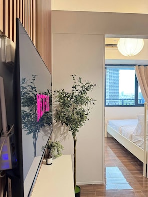 Ein modernes Hotelzimmer mit Bett, Fernseher, einer Topfpflanze und Blick auf die Stadt durch ein Fenster.
