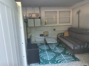 Ein kleiner, abgeschlossener Raum mit einer Couch, einem gemusterten Teppich und einem Fenster mit Jalousien.