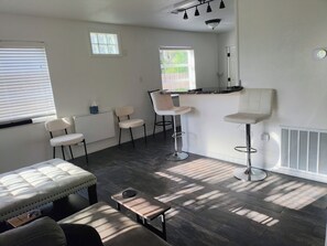 Ein modernes Wohnzimmer mit einer Couch, zwei Sesseln, einem kleinen Tisch und einer Küchenzeile mit einem Barhocker.