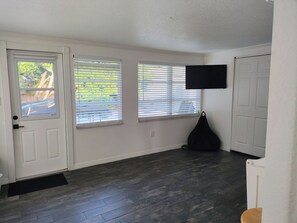 A room with a door, two windows with blinds, a black bag, and a television on the wall. - Duplex Near Beach, Bay, Recreational Park n Shops - 3-bedroom townhome (Bradenton)