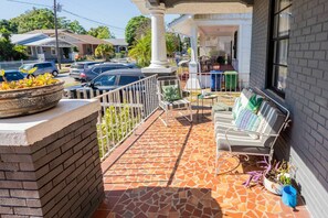 A covered outdoor seating area with a tiled floor, a white railing, and a brick wall. - Casa Grande | Historic 2BR Bungalow with Private Porch Near Ybor, Armature Works & Downtown Tampa (Tampa)
