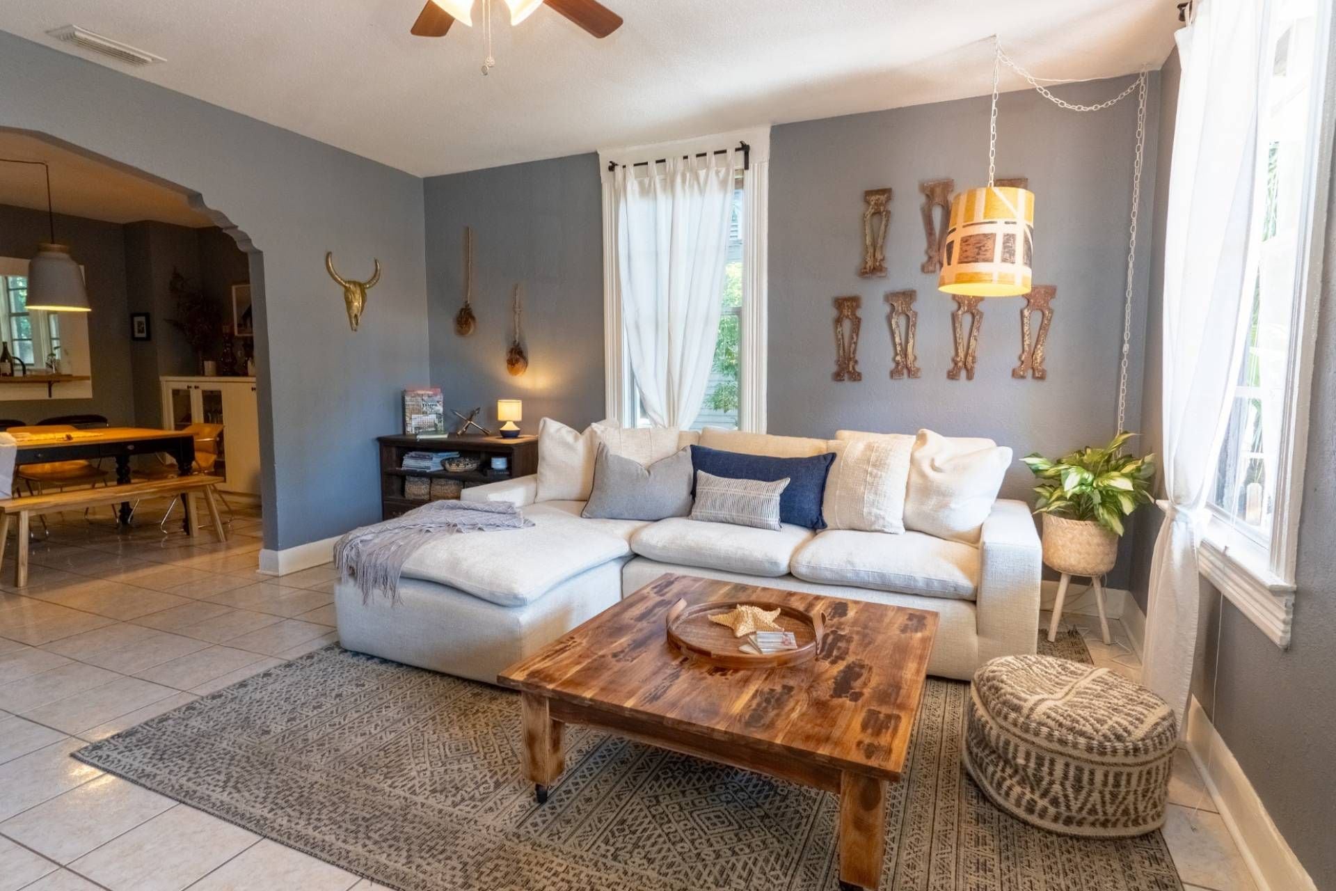 A living room with a sectional sofa, a wooden coffee table, a patterned rug, and a dining area with a bench.