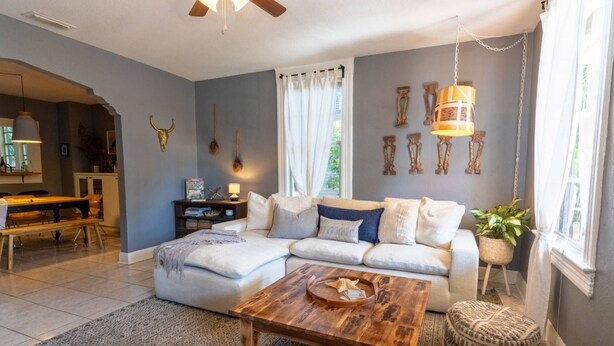 A living room with a sectional sofa, a wooden coffee table, a patterned rug, and a dining area with a bench. - Casa Grande | Historic 2BR Bungalow with Private Porch Near Ybor, Armature Works & Downtown Tampa (Tampa)