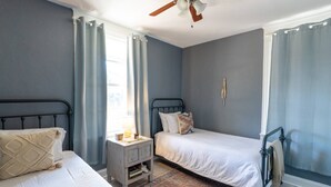 A bedroom with two beds, a nightstand, a ceiling fan, and a window with curtains. - Casa Grande | Historic 2BR Bungalow with Private Porch Near Ybor, Armature Works & Downtown Tampa (Tampa)