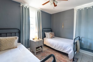 Ein Schlafzimmer mit zwei Betten, einem Nachttisch, einem Deckenventilator und einem Fenster mit Vorhängen.