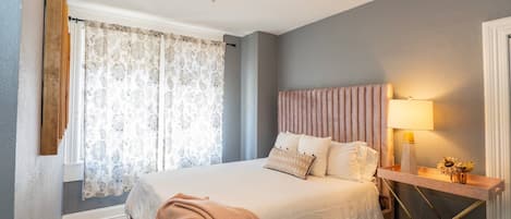 A bedroom with a bed, a ceiling fan, a bedside table with a lamp, and a window with curtains.