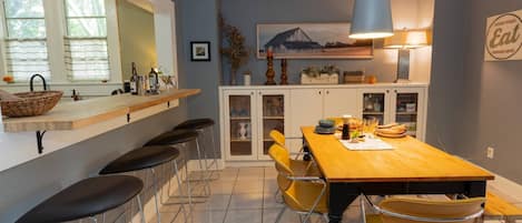 A kitchen with a wooden table, yellow chairs, a bar area with stools, and a hanging light fixture.