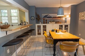 Eine Küche mit Holztisch, gelben Stühlen, einer Bar inklusive Hockern und einer Pendelleuchte.
