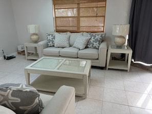 Ein Wohnzimmer mit einer Couch, zwei Beistelltischen, einem Couchtisch und einem Fenster mit Jalousien.