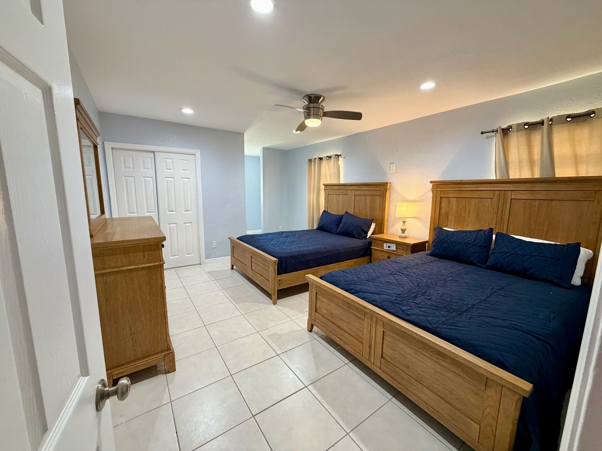 A hotel room with two wooden beds, a ceiling fan, and a door with a mirror.
