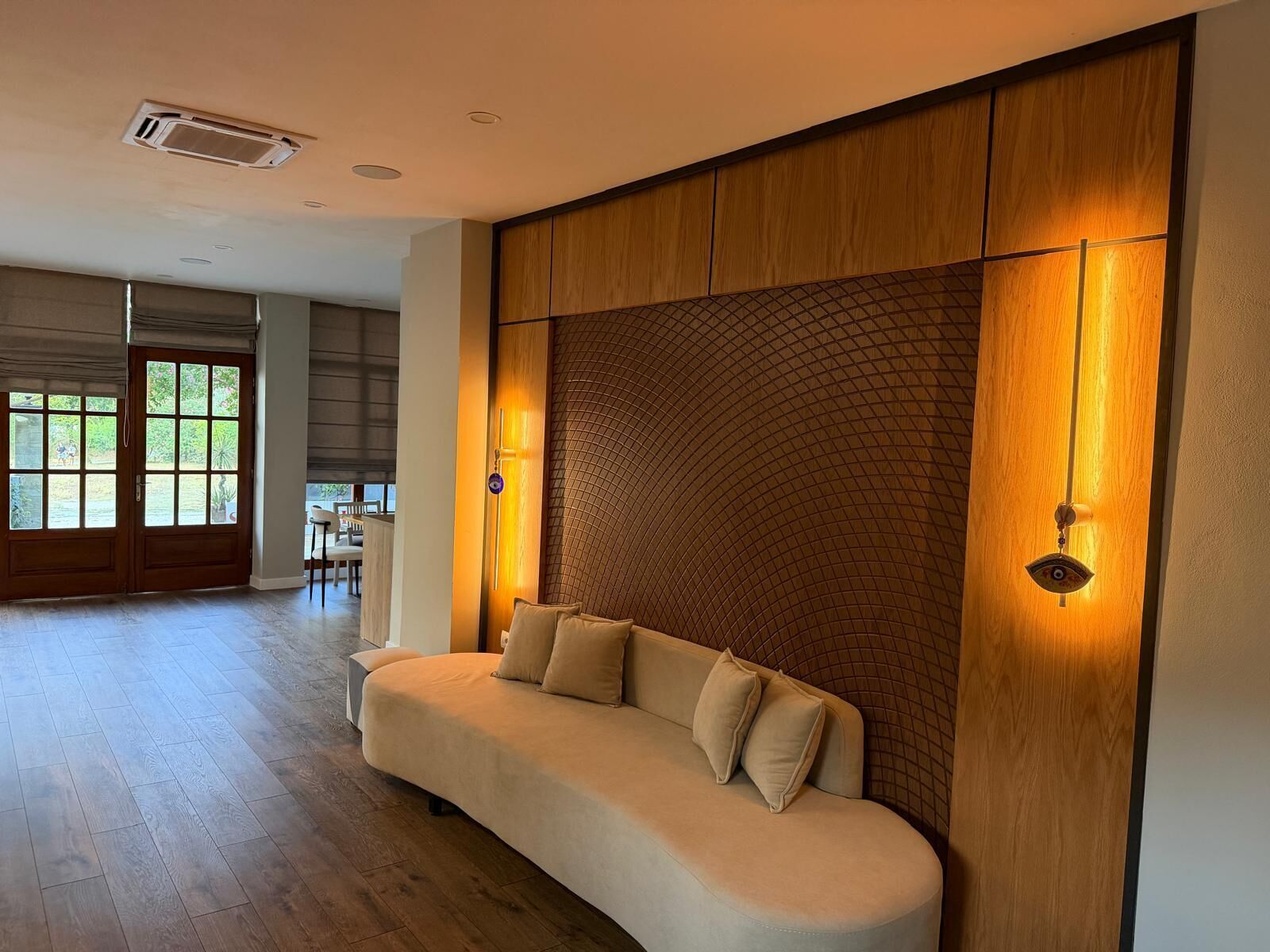 A modern living room with a curved sofa, wooden panel wall, and a view of the outdoors.