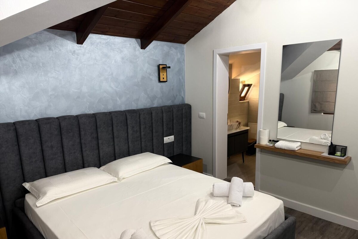 A bedroom with a large bed, a bedside table, a mirror, and a view into the bathroom.